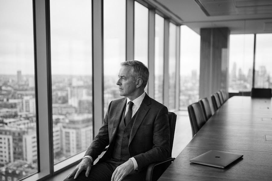 Chief executive turned away from a closed laptop at an empty boardroom table — boredom at the top